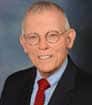 Male author smiling, wearing glasses, and a dark suit with a red tie